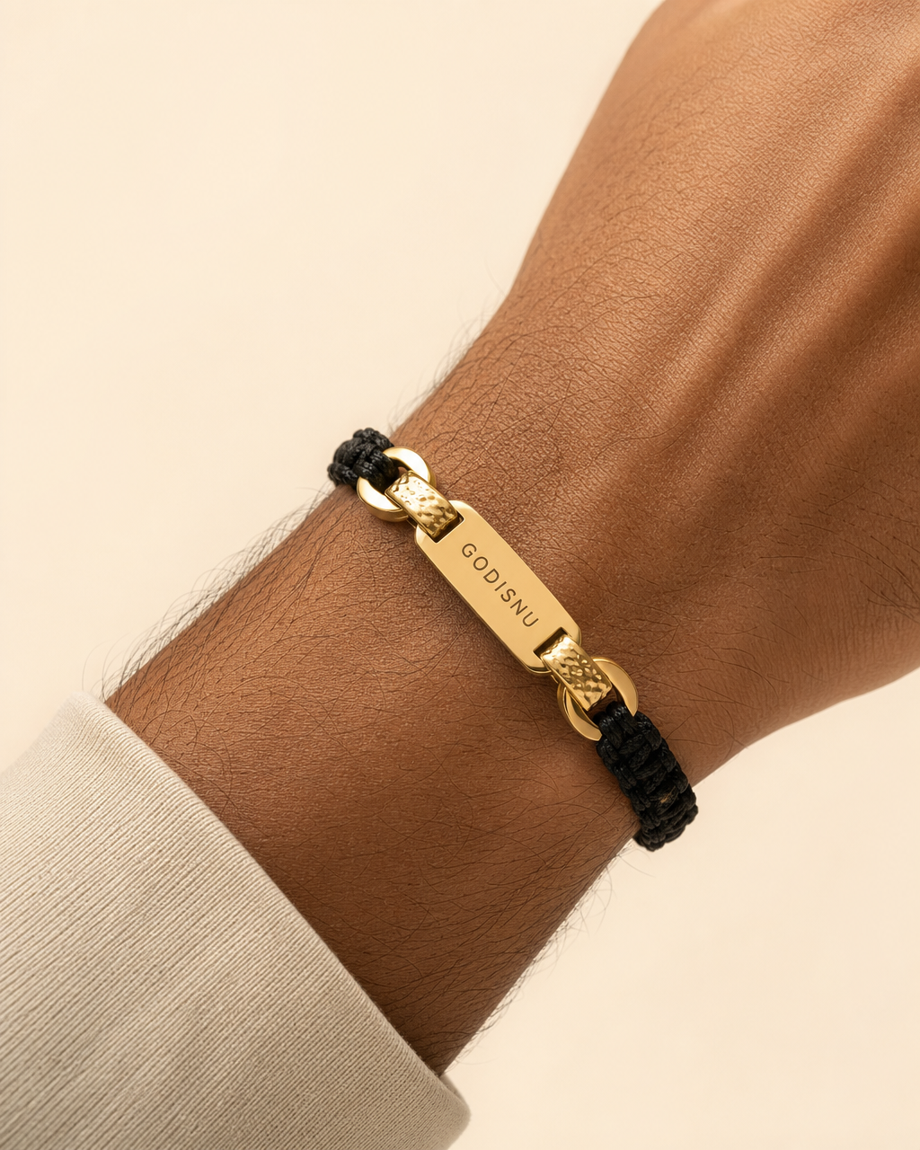 GODISNU woven black cord bracelet with gold GODISNU plate on a wrist